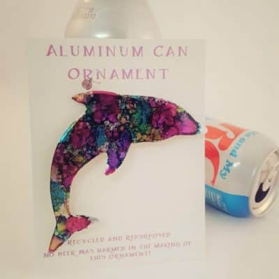 Colorfully painted aluminum dolphin ornament affixed to postcard that reads "Aluminum Can Ornament. Recycled and Repurposed. No beer was harmed in the making of this ornament!"